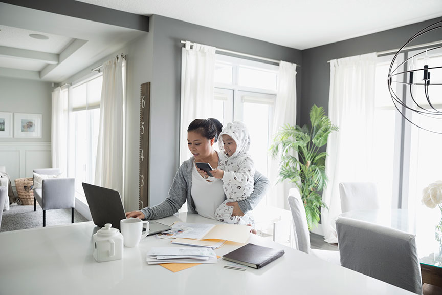 Mother doing finances on laptop while holding baby