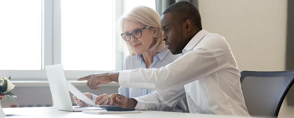 African american employee pointing at laptop discussing paperwork with colleague helping customer with laptop