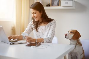 Woman using laptop with dog overlooking