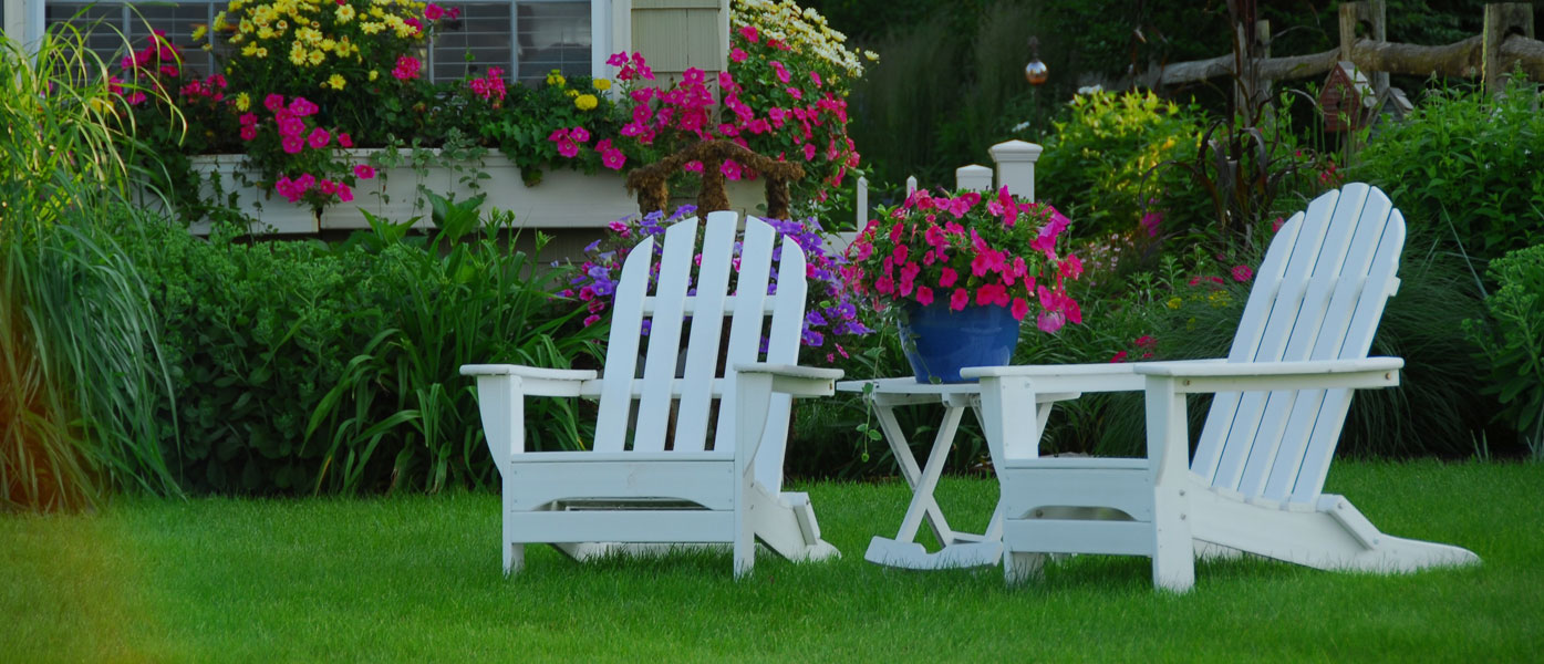 Pair of adirondack chairs on lush green lawn with spring landscaped house