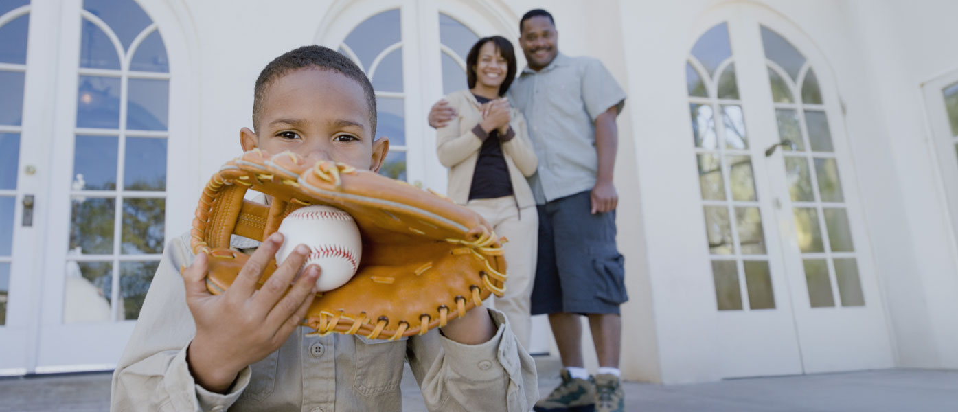 Young boy holding baseball mitt in front of house with parents