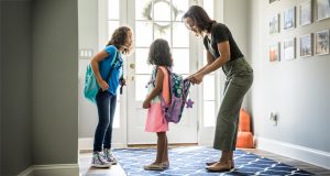 Mother helping two young daughters with their backpacks in the foyer of home