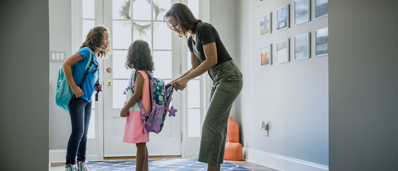 Mom helping children with backpacks in home